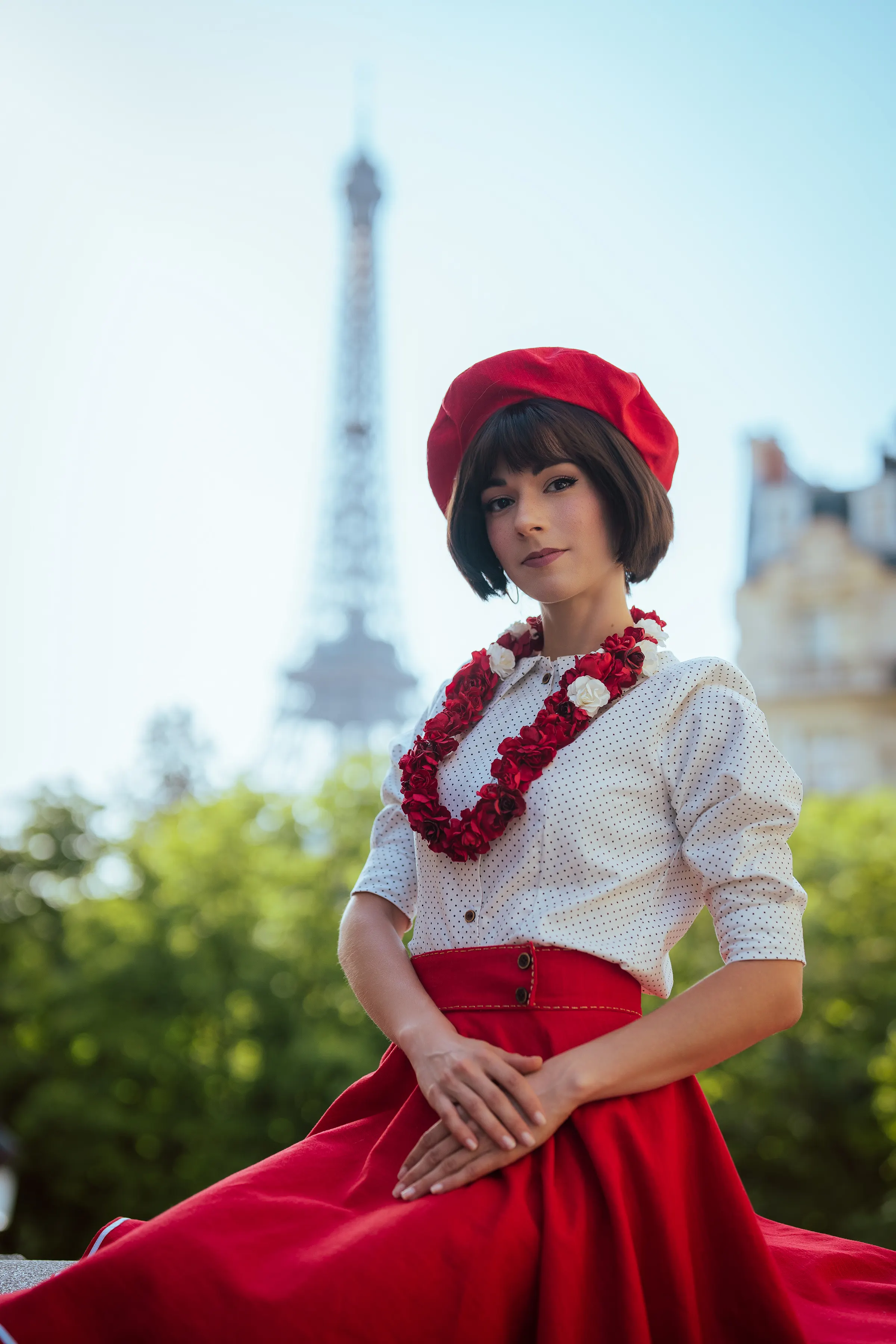 Sophie de Clair Obscur: Expédition 33, assise sur un muret, mains jointes, Tour Eiffel floutée en arrière-plan, cosplay Ryuu Seika